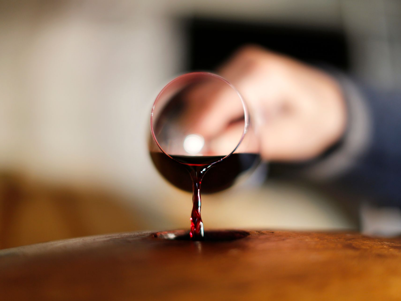 Du vin rouge se verse d'un verre sur un tonneau en bois.