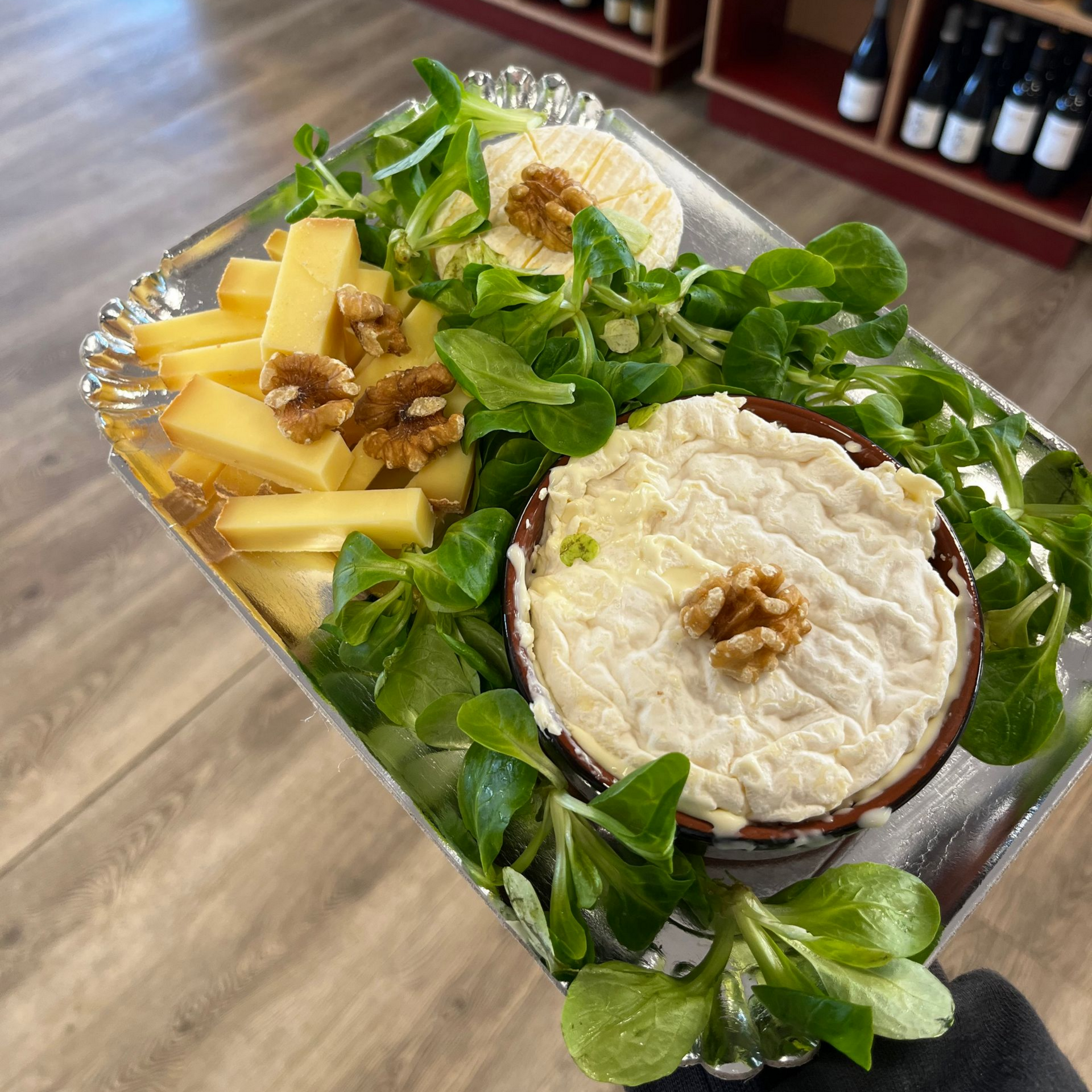 Assiette de fromages composée de fromage de chèvre, de cubes de fromage, de noix et de salade sur un plateau.