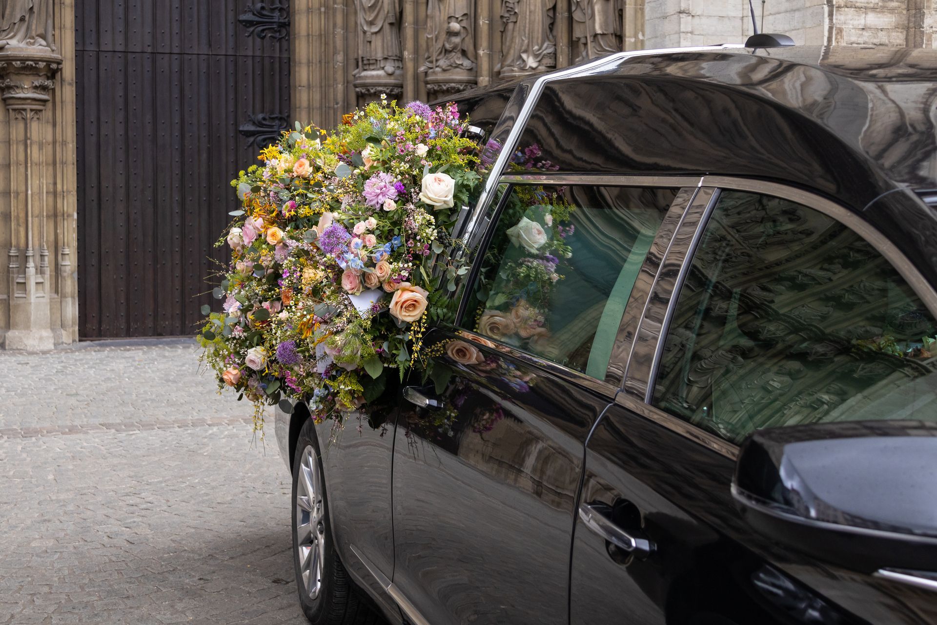 Un véhicule funéraire avec des fleurs devant une porte d'église