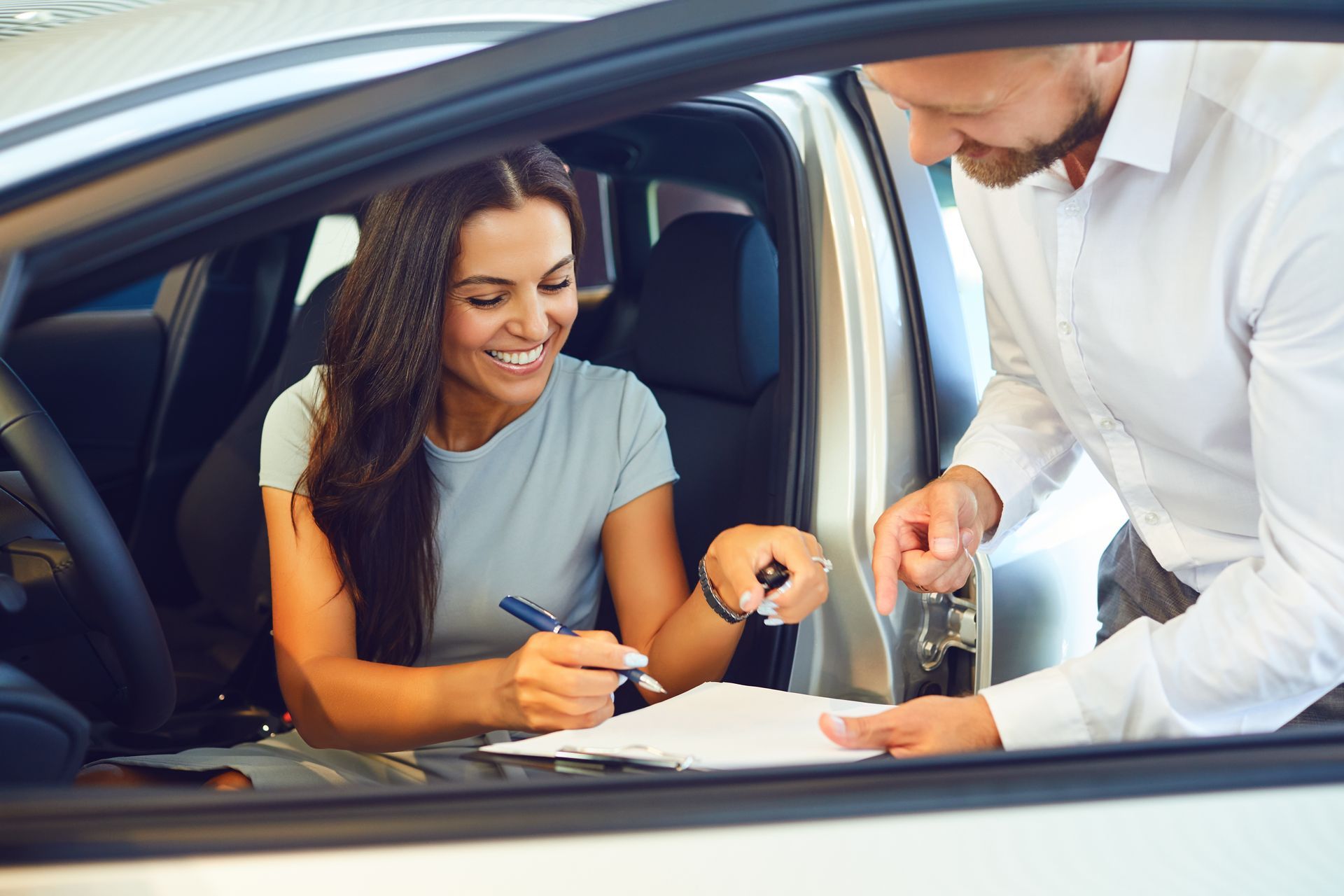Une femme signe des documents de voiture avec un vendeur dans une concession automobile.