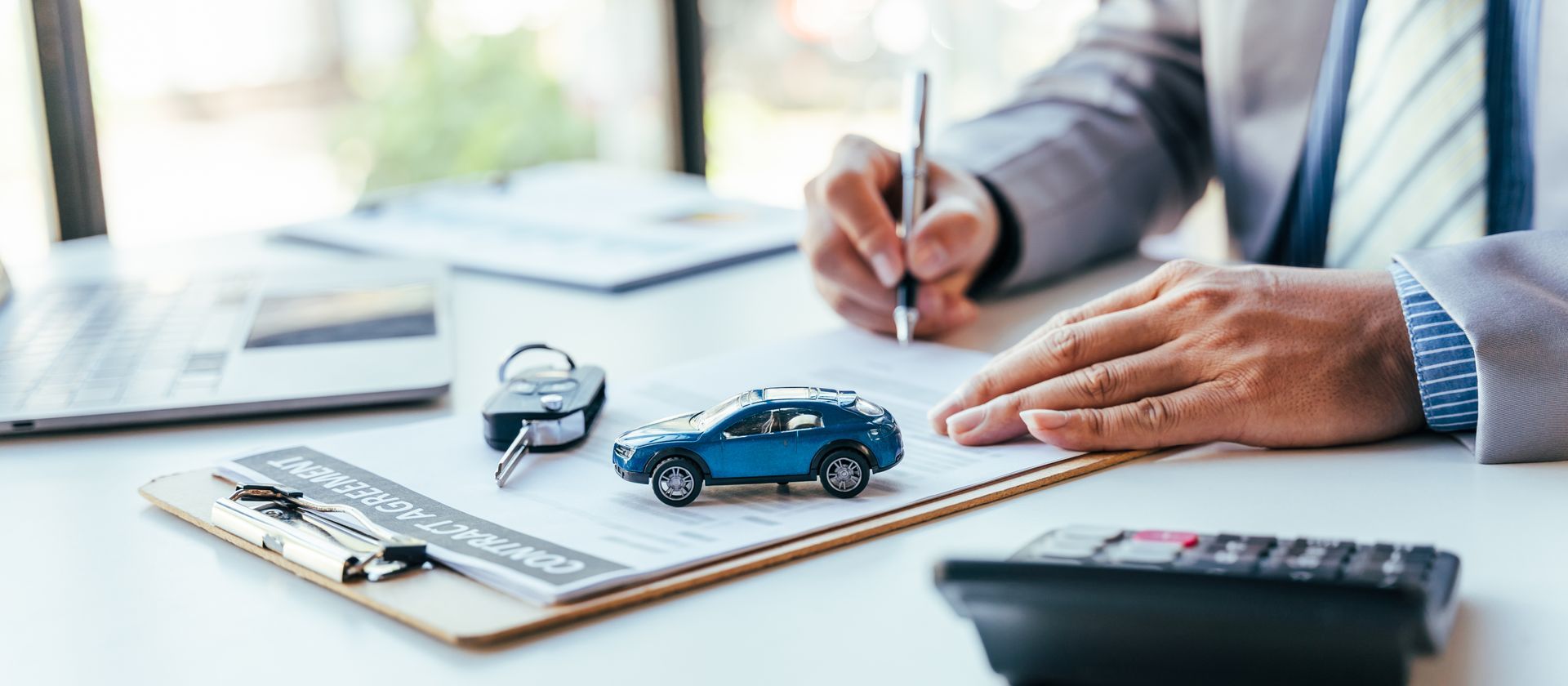 Une personne en costume écrit, avec des clés de voiture, une maquette de voiture et une calculatrice sur la table.