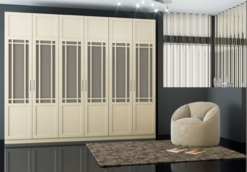 Dormitorio moderno con puertas de armario color crema, pared decorativa a rayas y silla beige junto a una alfombra oscura.