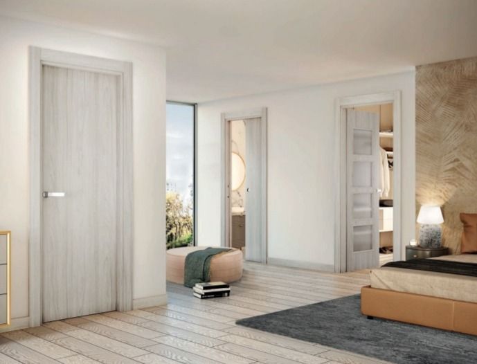 Dormitorio moderno de estilo minimalista con puertas de madera clara, alfombra gris, cama y lámpara de pared cálida junto a un sofá color canela.