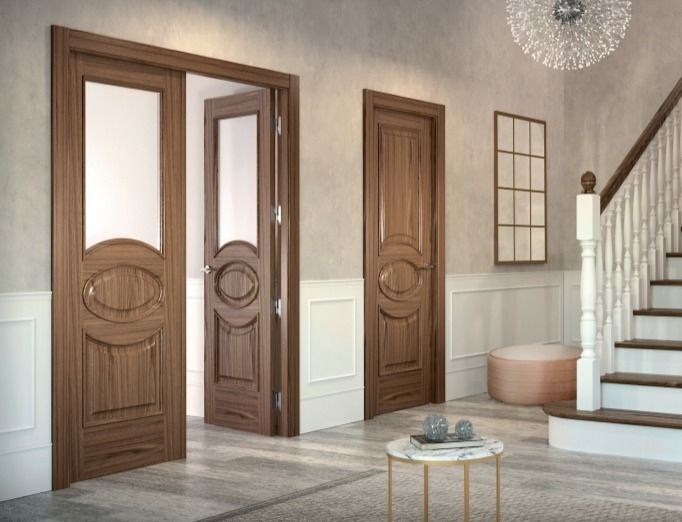 Entrada moderna con puertas de madera, escalera, otomana redonda y una mesita sobre un suelo gris.