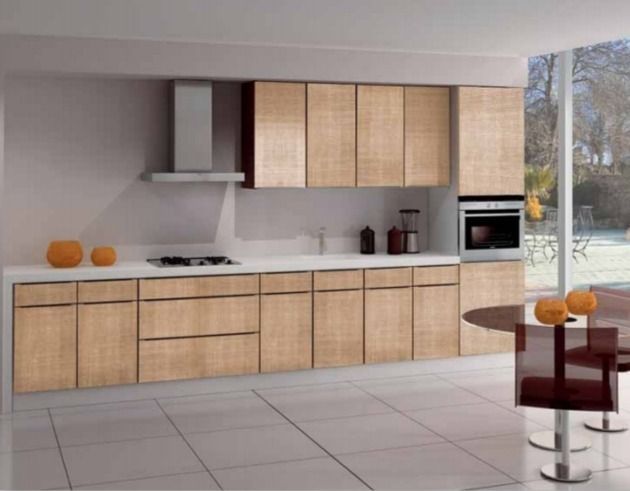 Cocina moderna con armarios de madera clara, encimeras blancas, suelo de baldosas y ventana con vistas al exterior.
