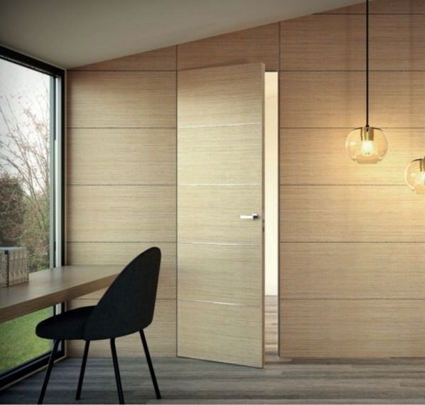 Habitación minimalista de madera con una silla negra junto a la ventana y dos lámparas colgantes.