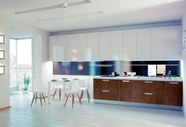 Cocina moderna blanca con isla, mesa de comedor y armarios bajos de madera en una habitación luminosa y diáfana.