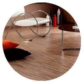 Sala de estar moderna con mesa de centro circular de cristal y suelo de madera, además de cojines y botellas decorativas.