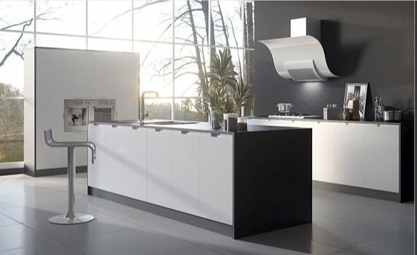 Cocina moderna blanca con isla, fregadero y taburetes cromados, iluminada por la luz natural que entra a través de grandes ventanales.