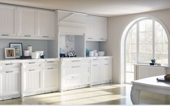Cocina blanca y luminosa con armarios, encimera decorada y una ventana arqueada que deja entrar la luz del sol.