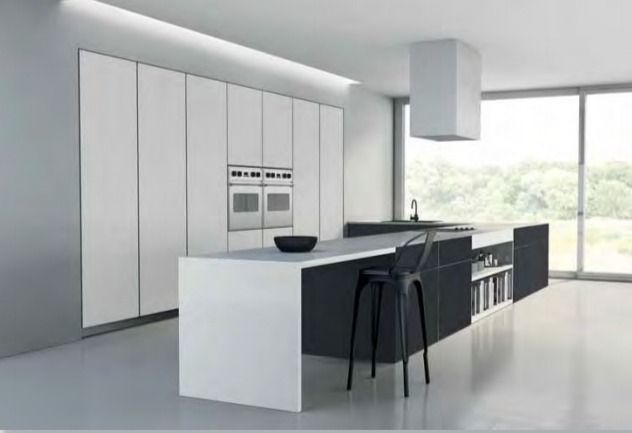 Cocina moderna minimalista blanca con isla, taburetes de bar, hornos empotrados y grandes ventanales.