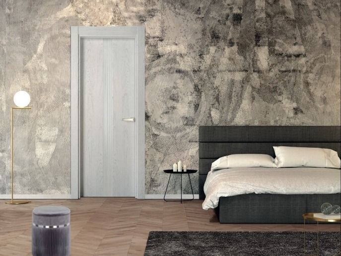 Dormitorio moderno con pared texturizada gris, puerta blanca, cama baja, lámpara de pie y suelo de madera.