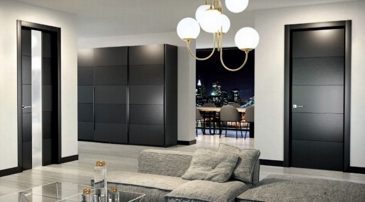 Sala de estar moderna con paneles de pared oscuros, lámparas colgantes, sofá gris y vista a la ciudad por la noche.