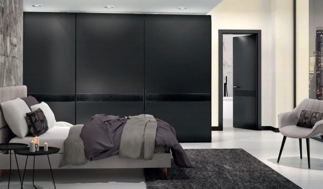 Dormitorio moderno con armario negro, cama gris y sillas blancas sobre una alfombra oscura.