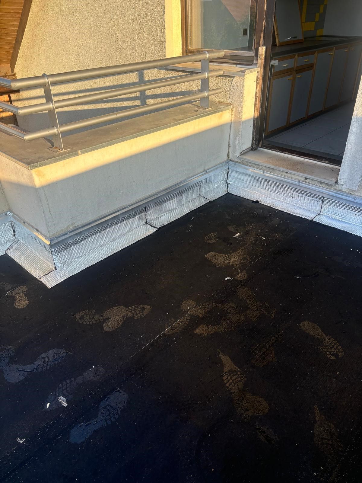 Toit plat à surface noire. Rambarde et bordure argentées. Empreintes de pas visibles.