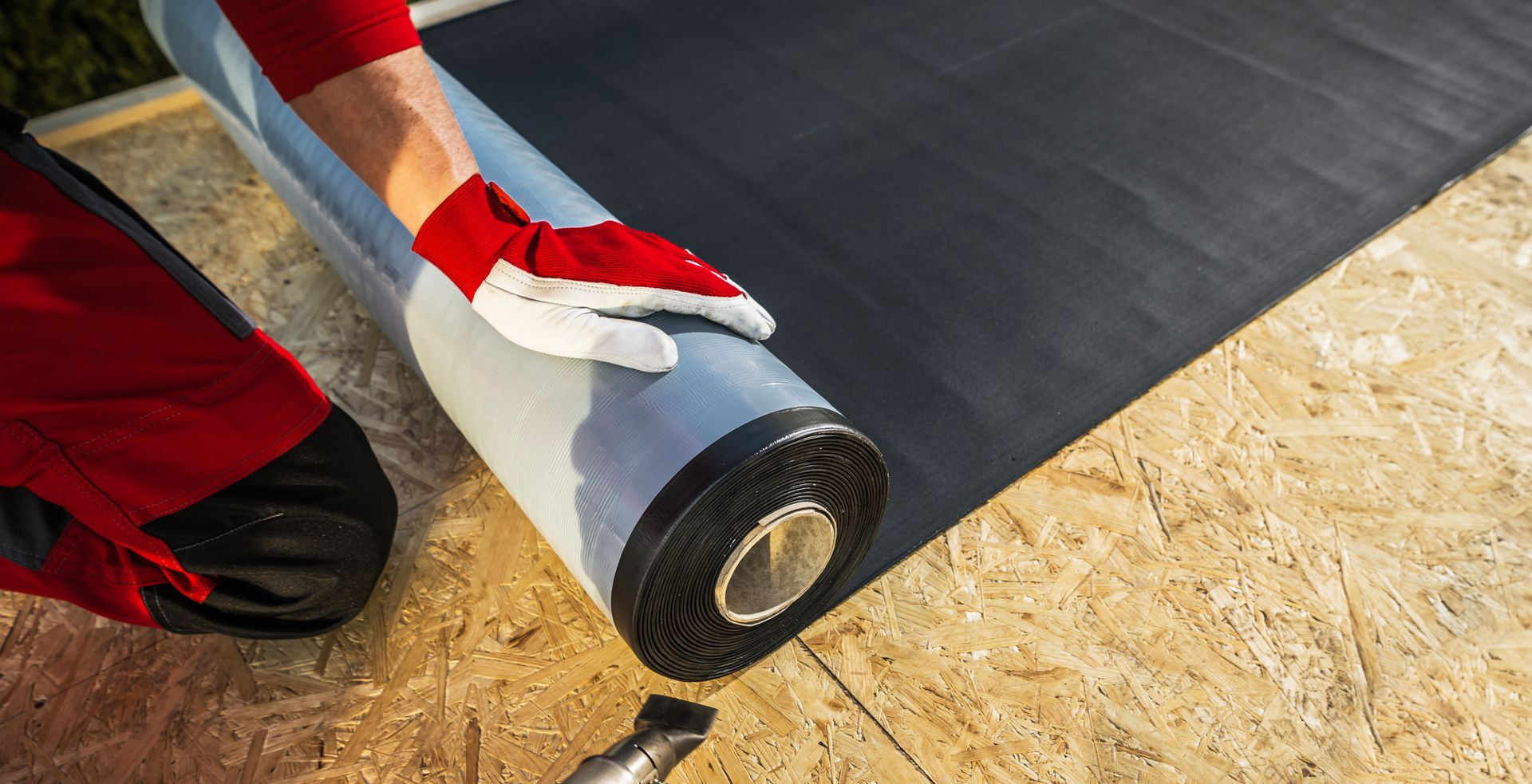 Personne installant une membrane d'étanchéité sur une surface en bois, portant des gants.