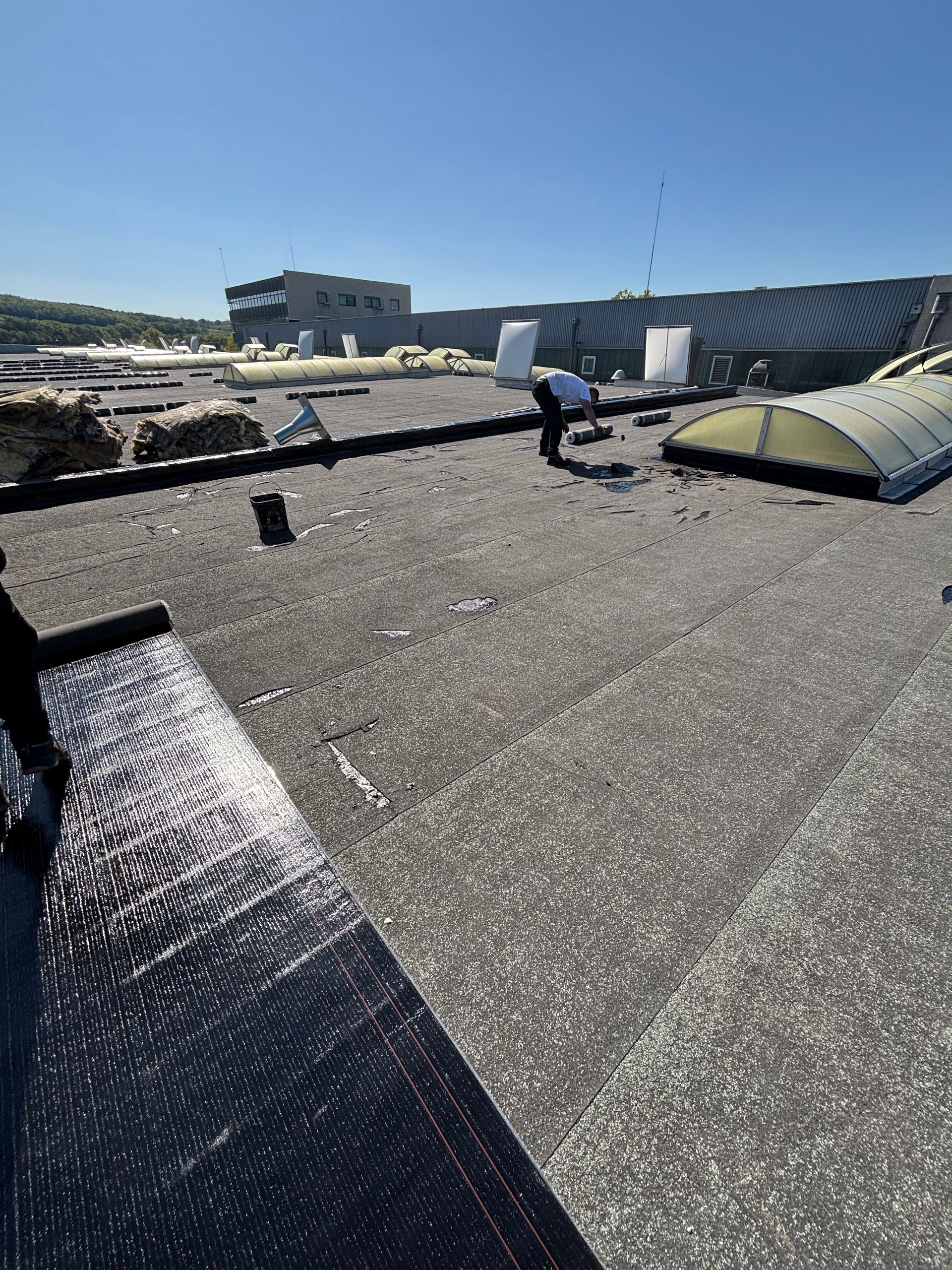 Des travaux sont en cours sur un toit noir sous un ciel bleu, une personne inspectant la surface.