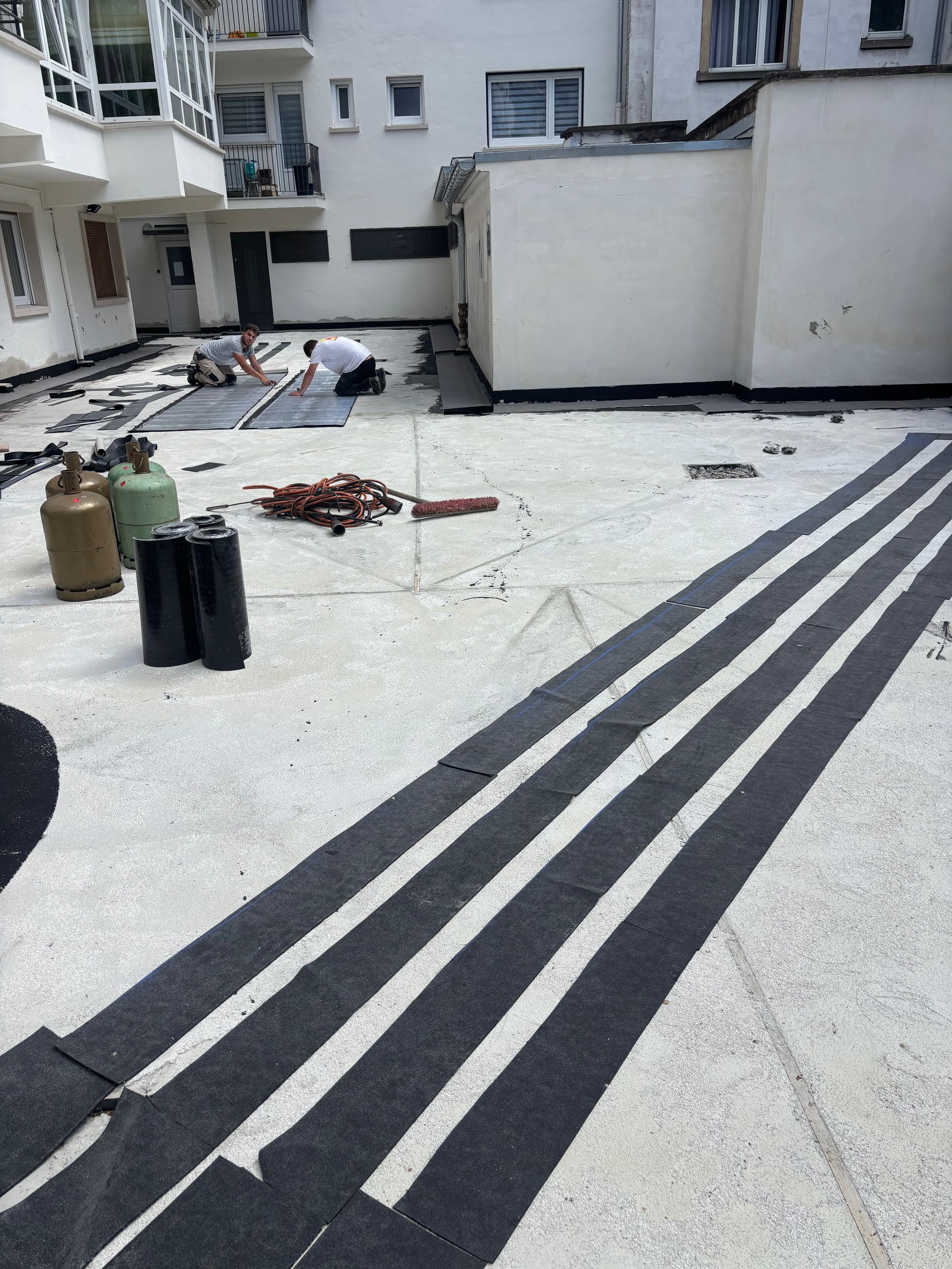 Travaux de toiture en cours : des hommes installent des bandes noires sur un toit plat.