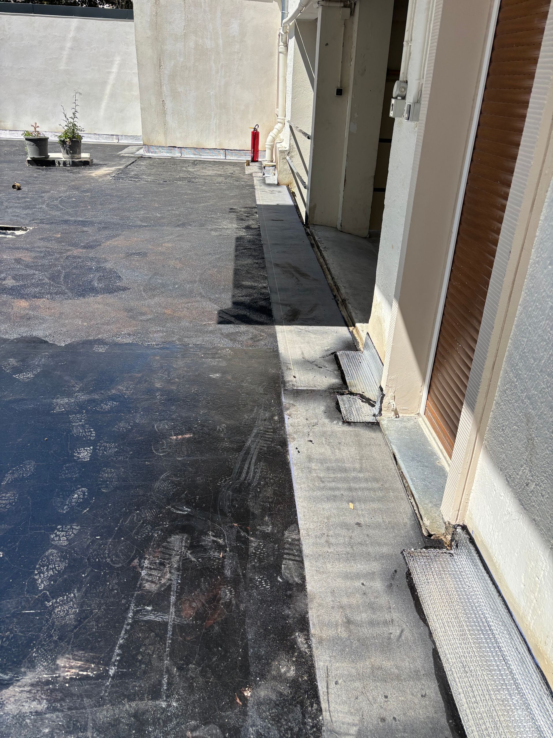 Toit plat noir avec bordure en béton gris clair, jouxtant un bâtiment. Zone ensoleillée.