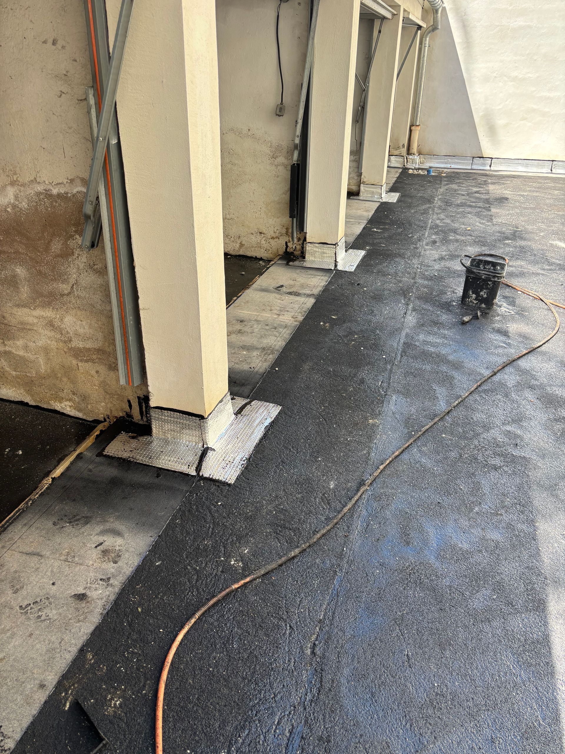 Sol sombre et texturé avec colonnes de soutien. Un tuyau d'arrosage et du petit matériel sont également présents.