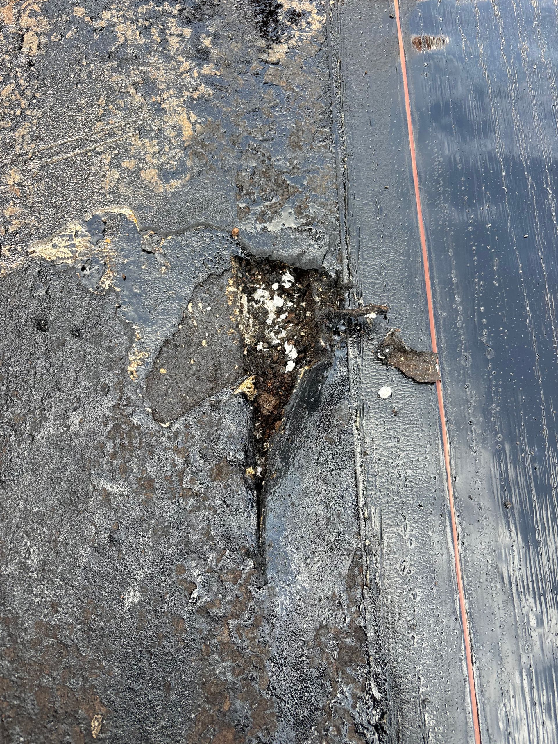 Partie endommagée d'un toit plat noir, présentant des couches exposées, de la saleté et des dégâts des eaux.