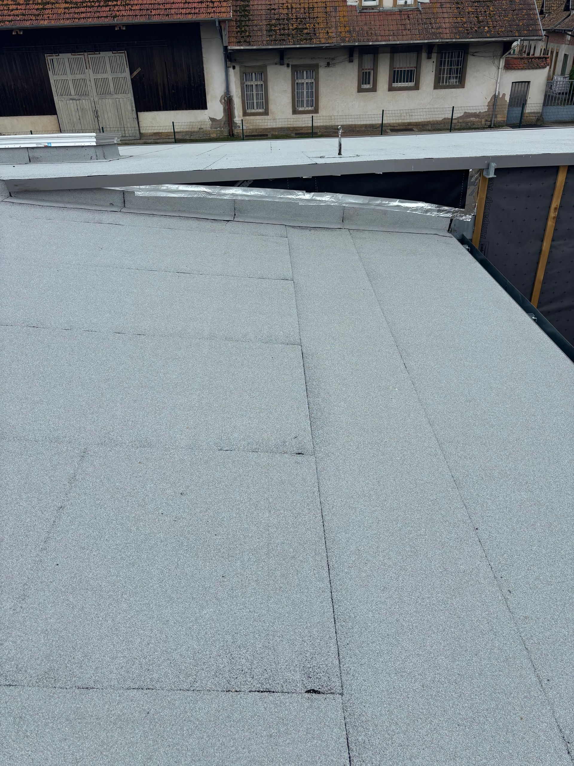 Un toit plat, gris et recouvert de gravier, avec des bâtiments en arrière-plan.