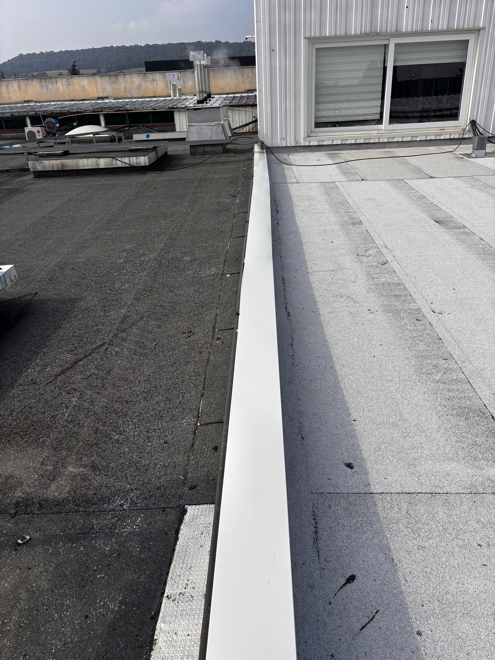 Vue depuis un toit. Un côté est recouvert de gravier noir, l'autre d'une membrane blanche, séparés par un mur blanc.