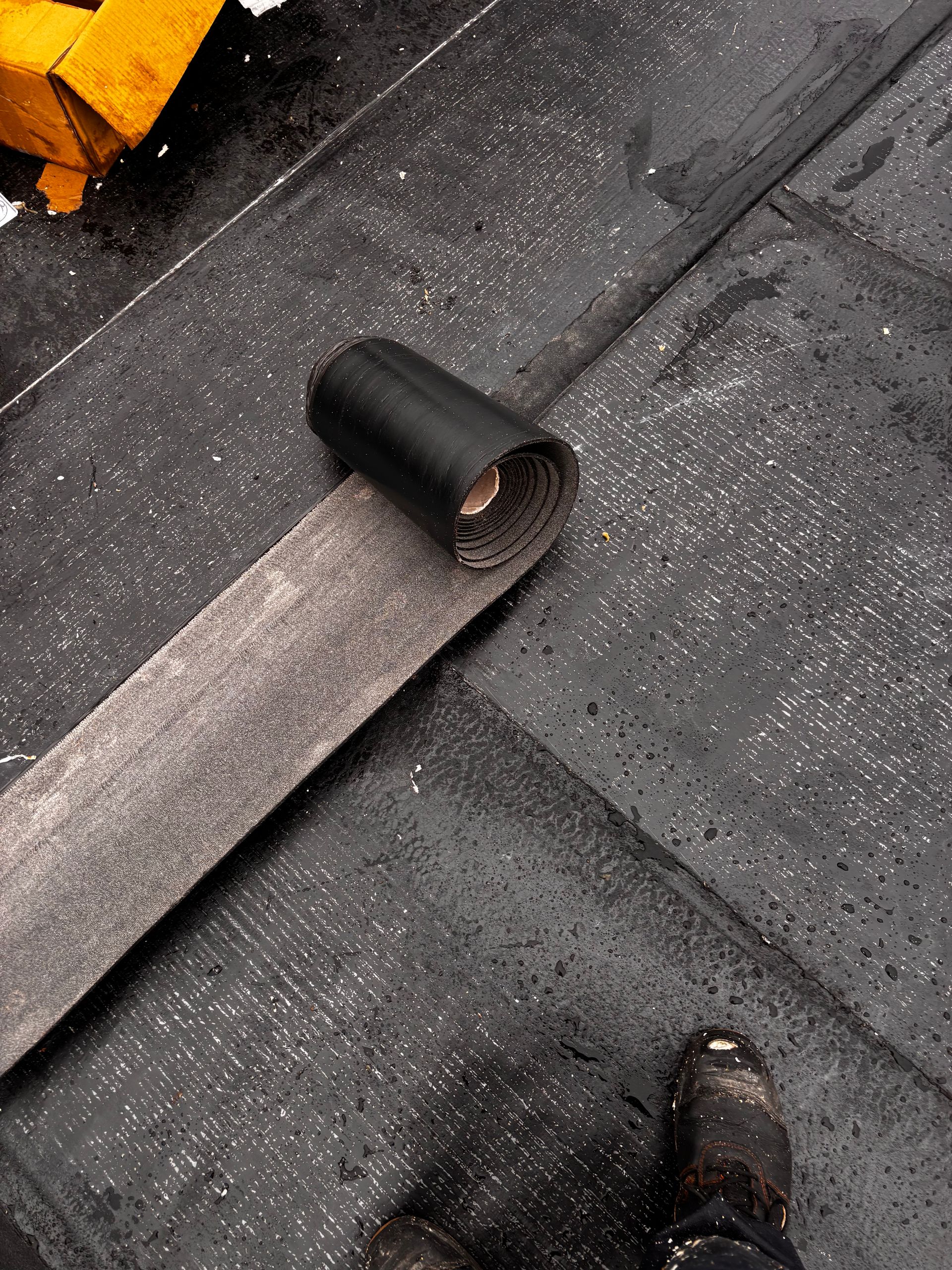 Tuyau noir et bande grise sur une surface sombre et texturée ; un pied est visible.