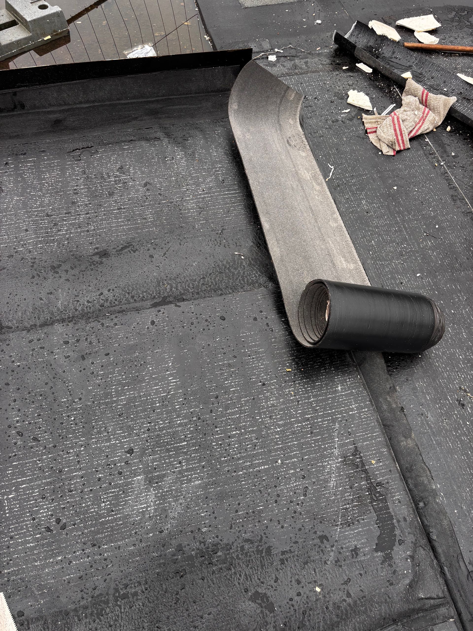 Rouleau de matériau de toiture noir sur une surface sombre, partiellement déroulé.