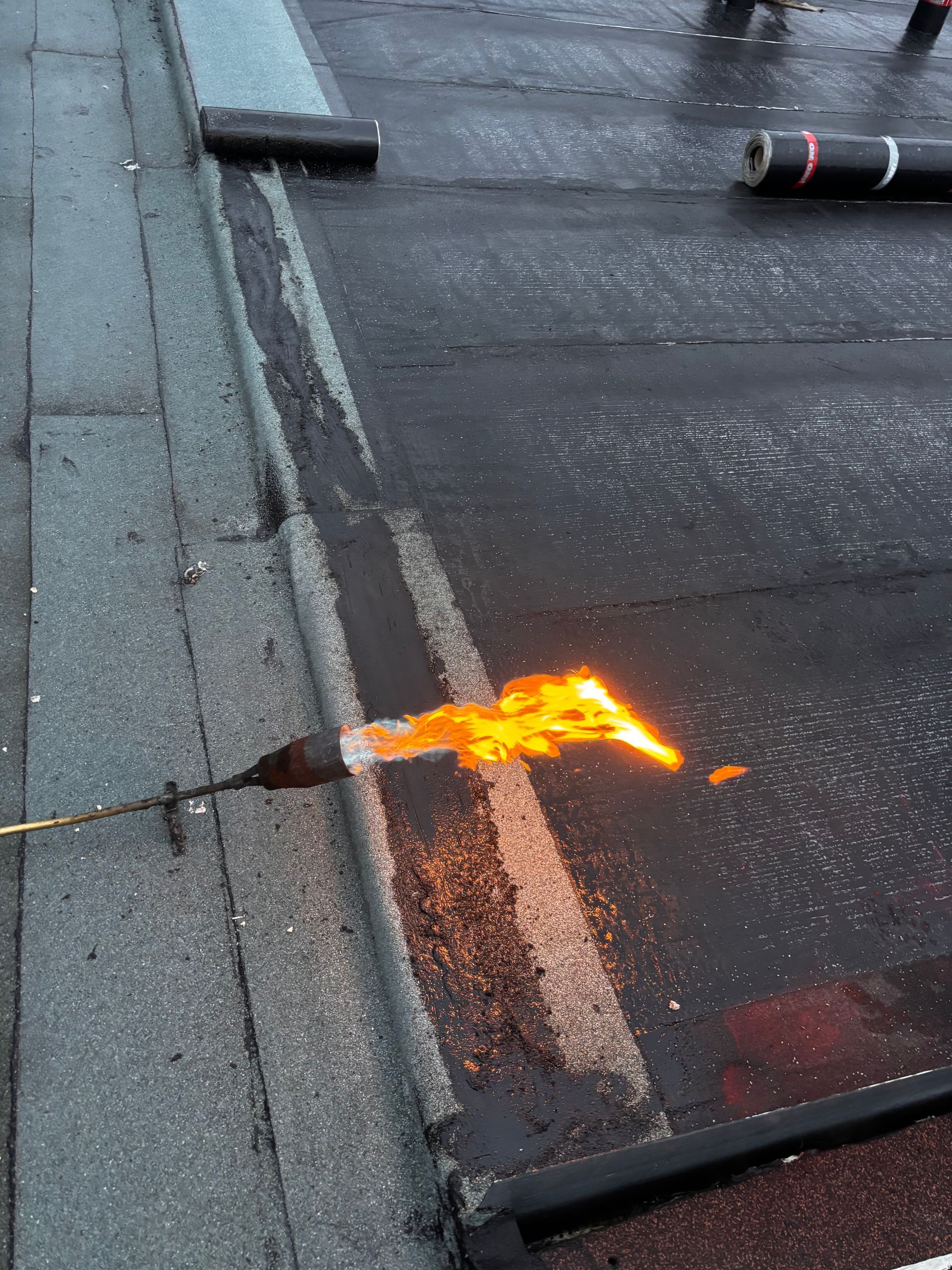 Application de l'enduit de toiture au chalumeau. Les flammes chauffent l'asphalte sur un toit noir.