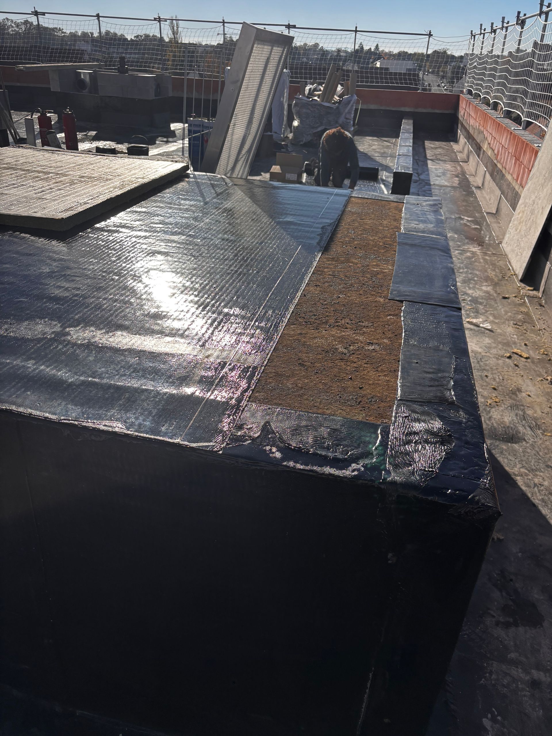 Toit plat recouvert d'un enduit réfléchissant foncé et d'une bande de gravier. Chantier de construction avec grues visibles en arrière-plan.