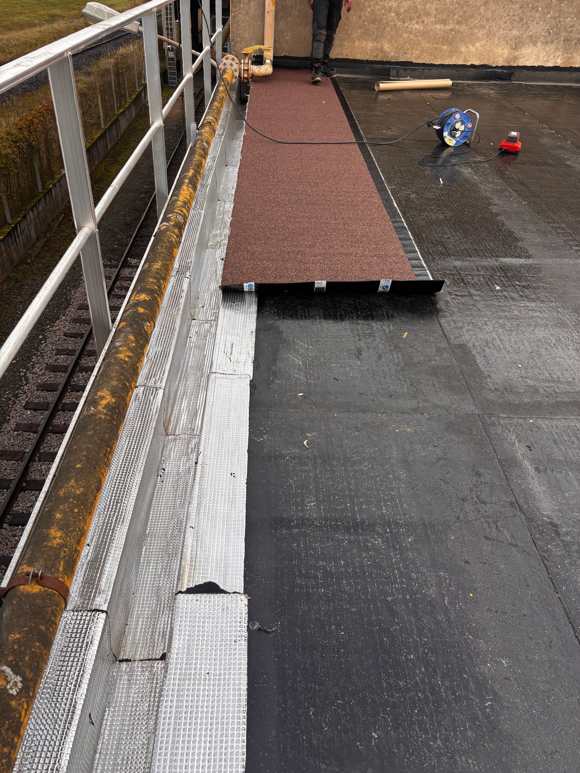 Bord de toit plat avec garde-corps, montrant les matériaux de toiture et la construction en cours.