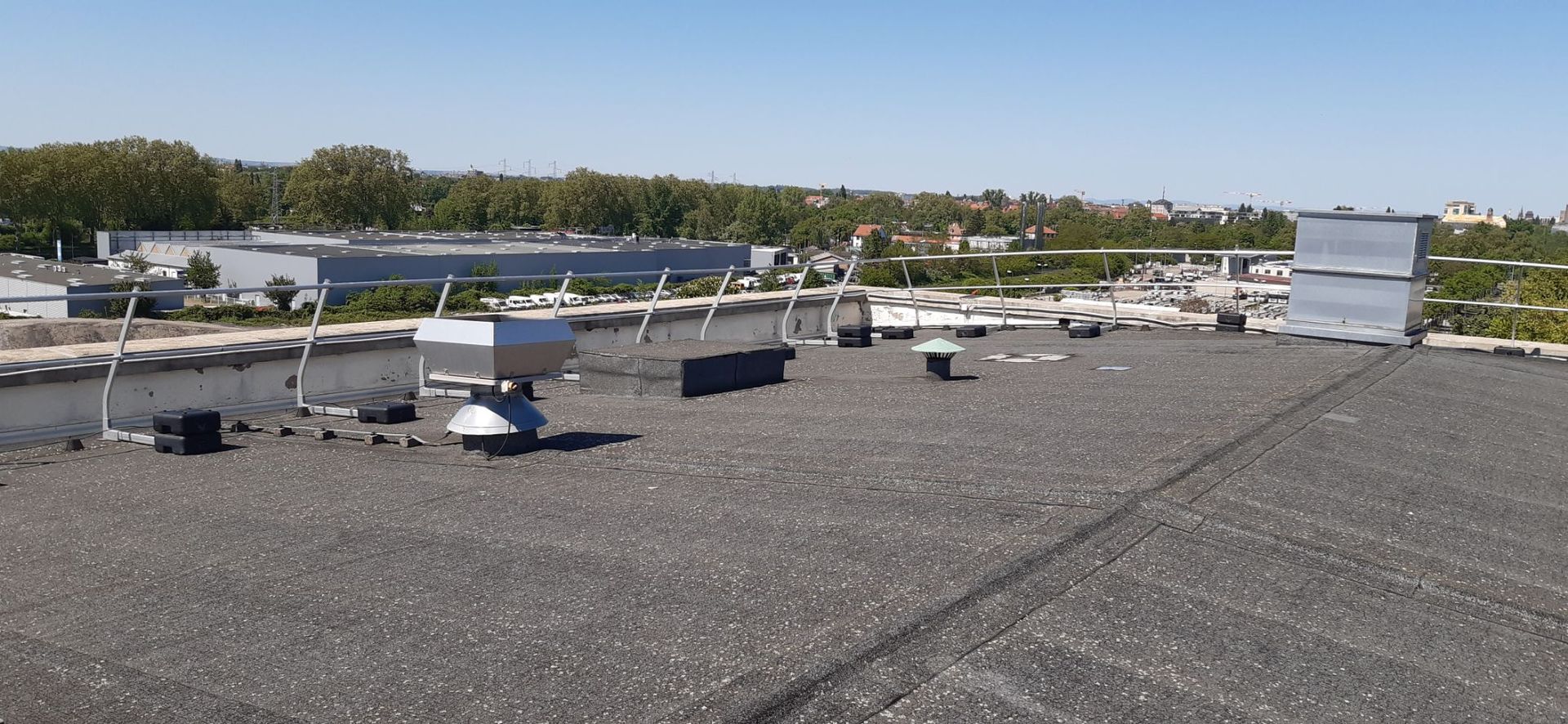 Un toit-terrasse avec divers équipements, des arbres en arrière-plan, par une journée ensoleillée.