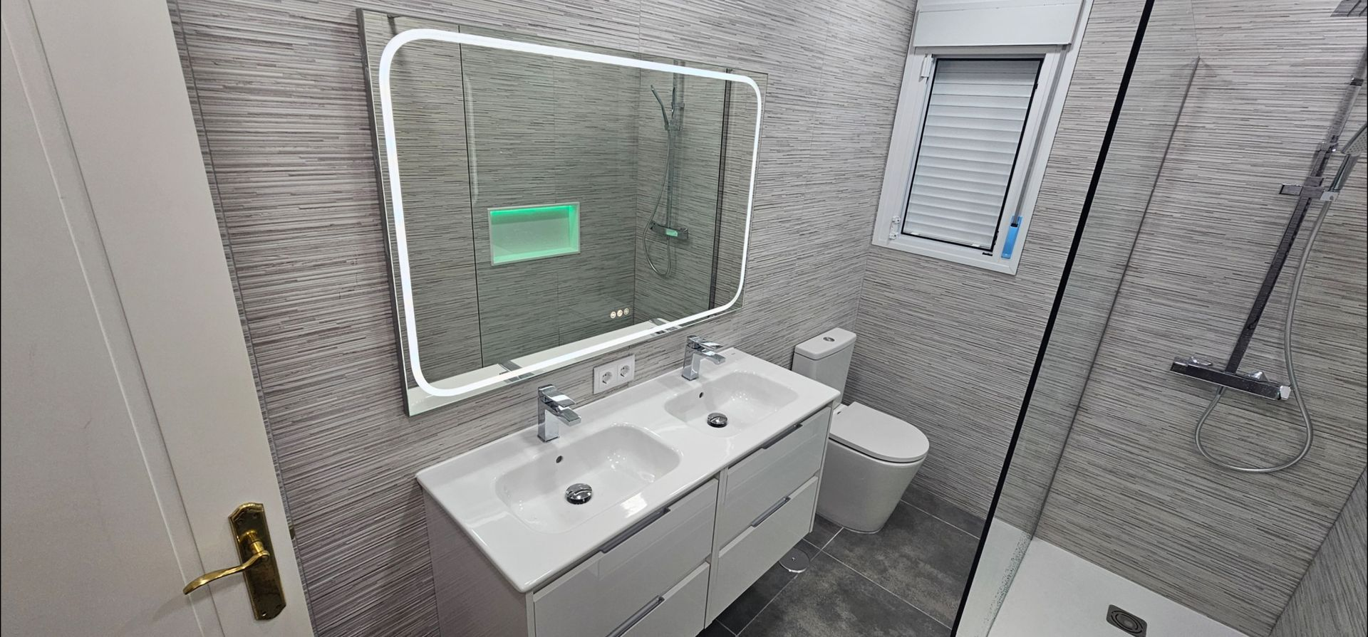 Baño moderno con tocador con dos lavabos, espejo iluminado y ducha a ras de suelo.