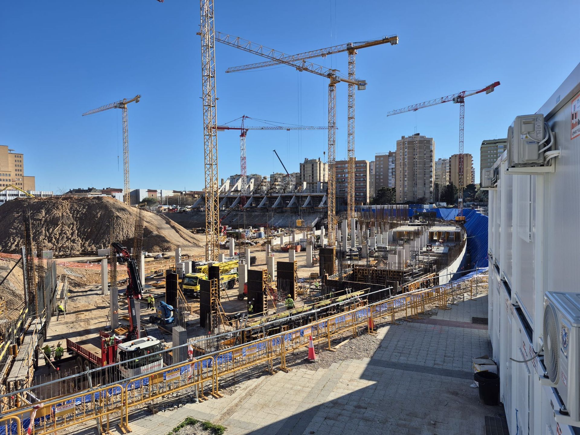 Obreros de la construcción con chalecos naranjas atando barras de refuerzo en la obra de cimentación de un edificio.