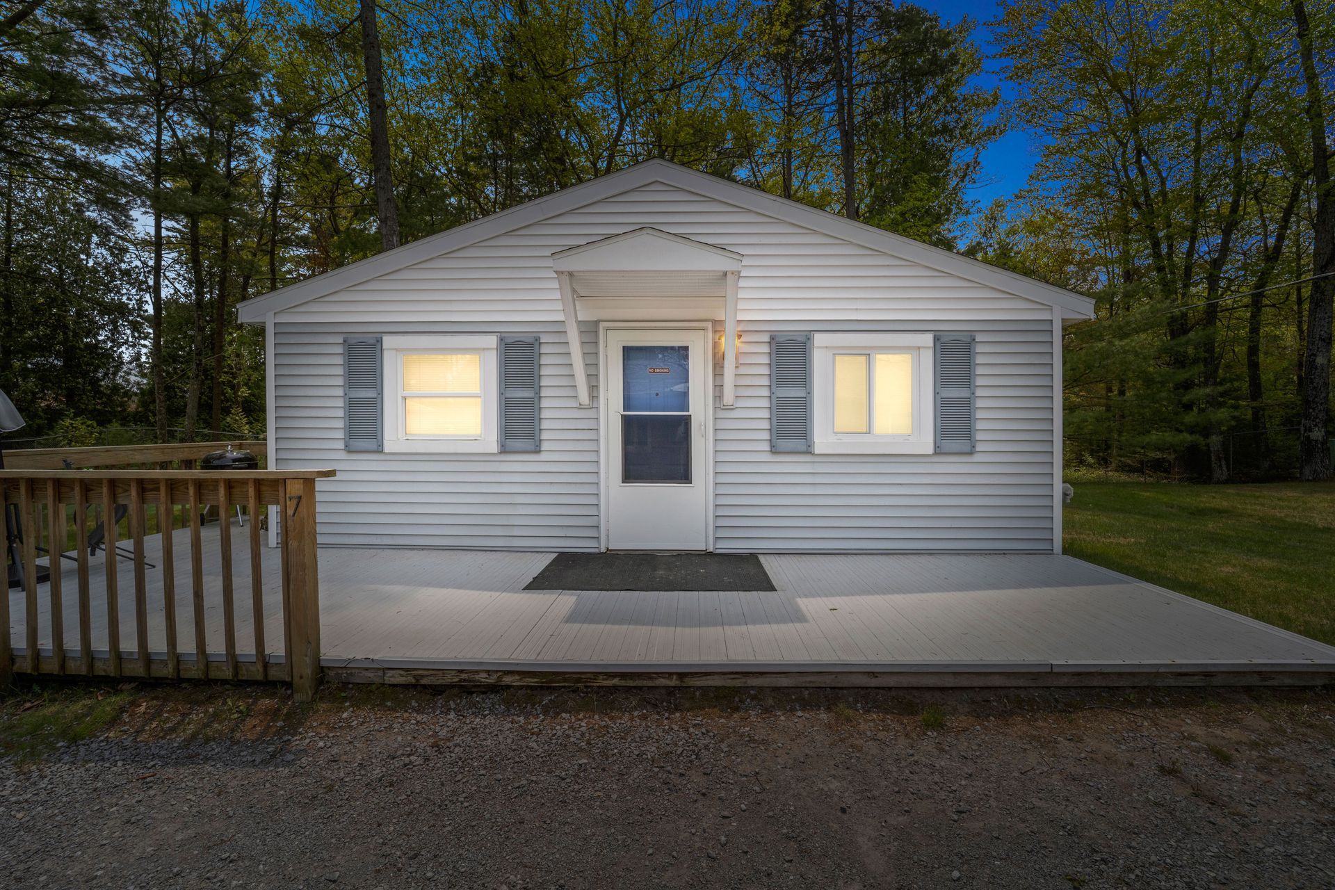 A small white house is sitting in the middle of a grassy field surrounded by trees.