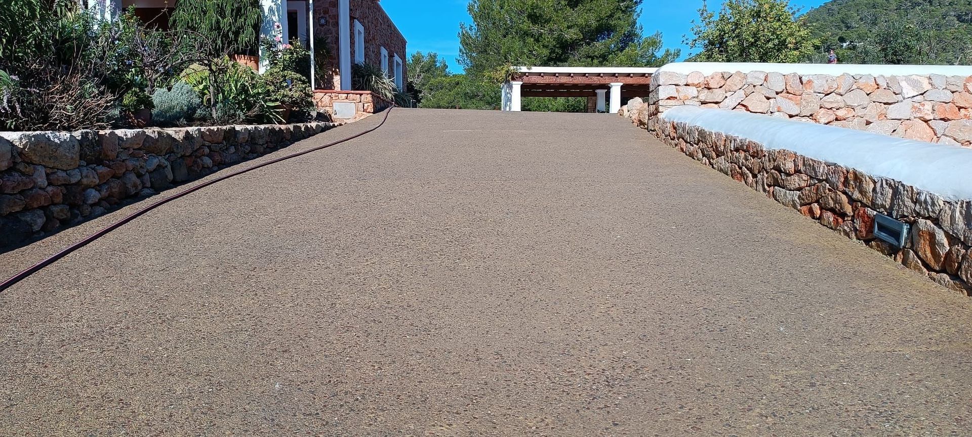 Un camino de entrada que conduce a una casa con un muro de piedra al costado.