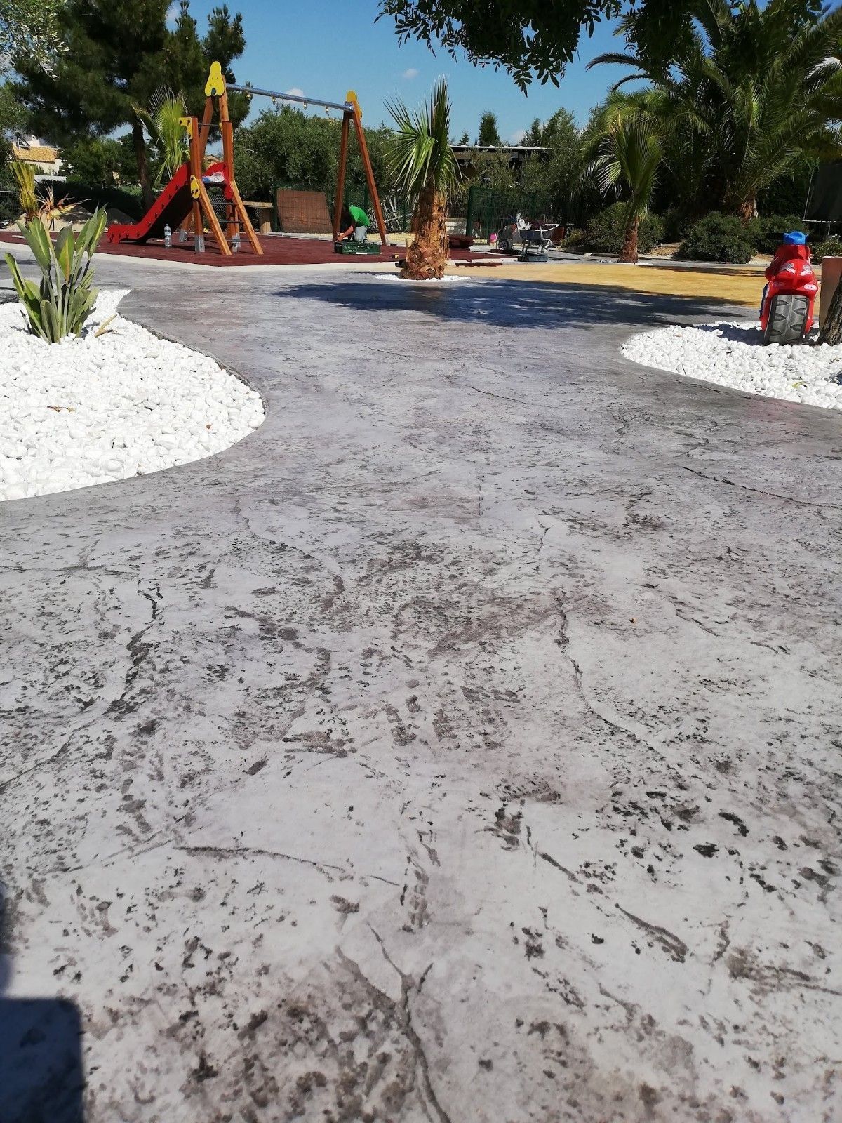 Un camino de entrada de hormigón con un parque infantil al fondo.