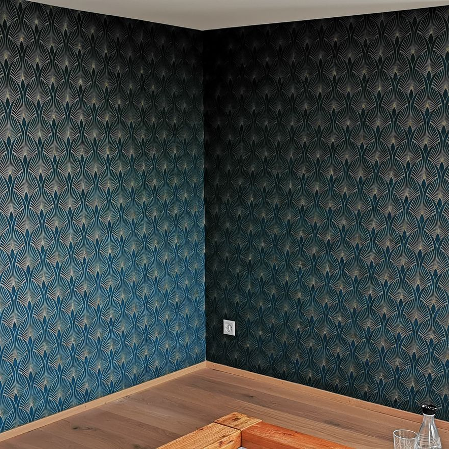 Eine Wand mit Steinoptik und daran befestigtem schwarzen Gerät, ein Fenster mit Lamellenjalousien und eine Topfpflanze in einem Zimmer.