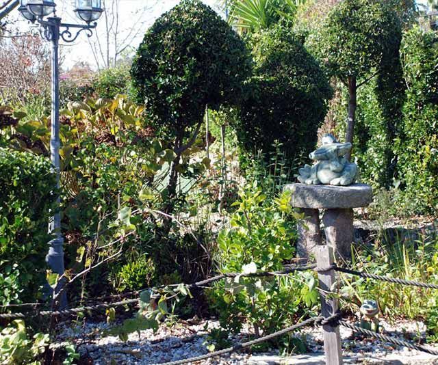 Una estatua de una rana se sienta encima de una fuente en un jardín.