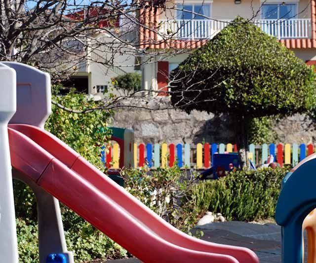 Un tobogán en un parque infantil con una casa al fondo.