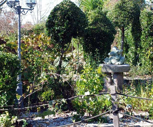 Una estatua de una rana se sienta encima de una fuente en un jardín.