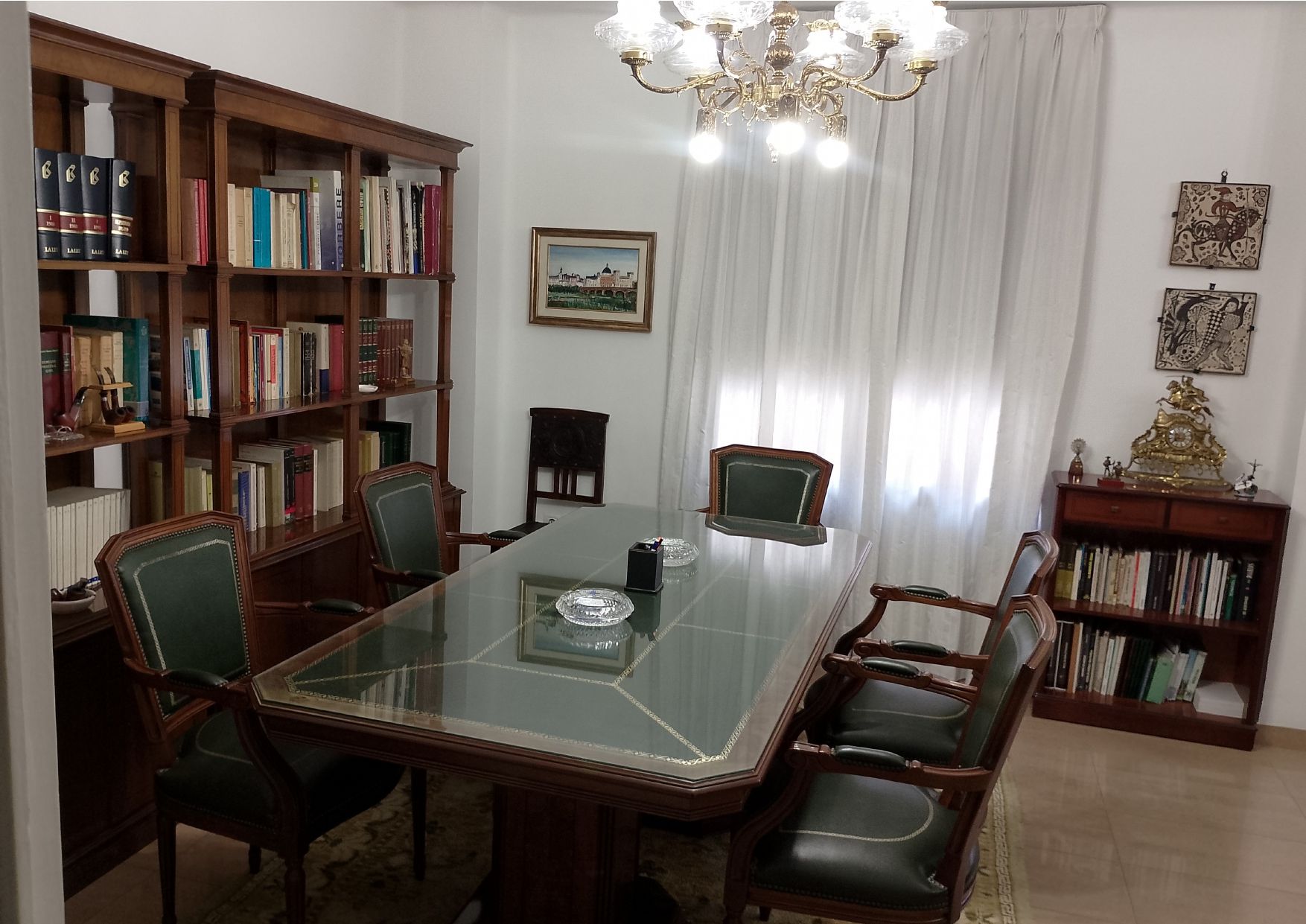 Oficina con escritorio de madera oscura, sillas, estanterías y lámpara de araña.