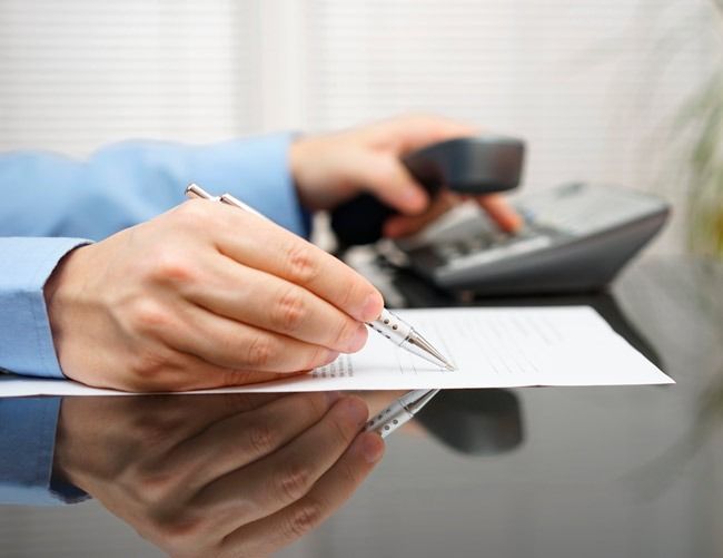 Una persona está escribiendo en un trozo de papel mientras habla por teléfono.