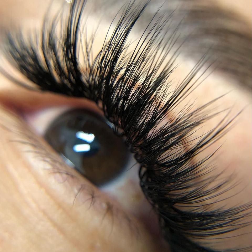 Primer plano de un ojo con extensiones de pestañas densas, largas y negras, de textura suave y ligera.