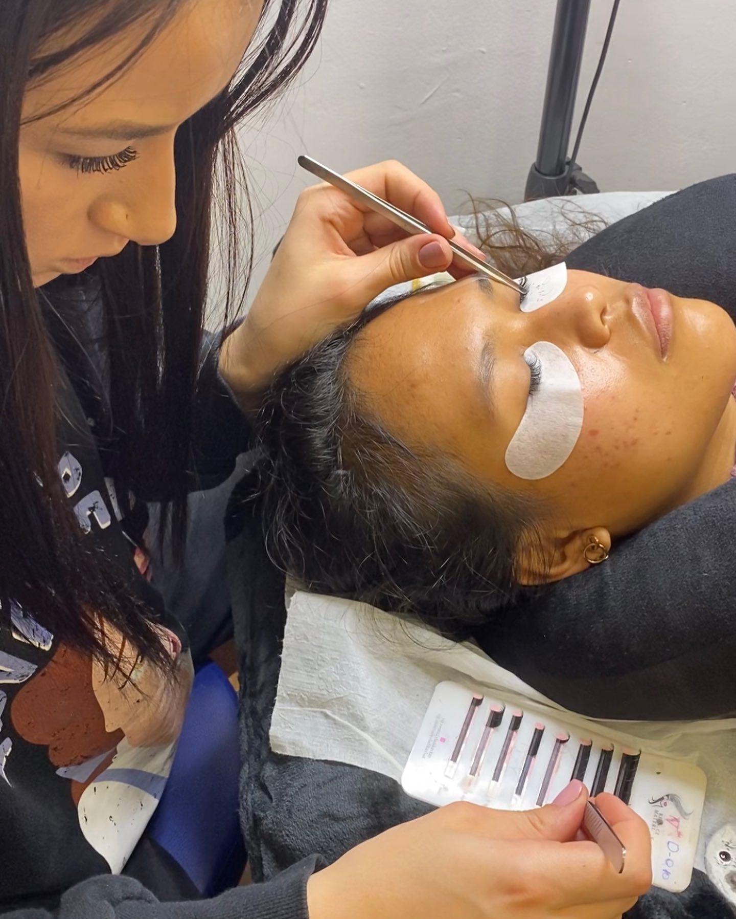 Una técnica de pestañas aplica extensiones de pestañas a una clienta que está tumbada con almohadillas para los ojos.