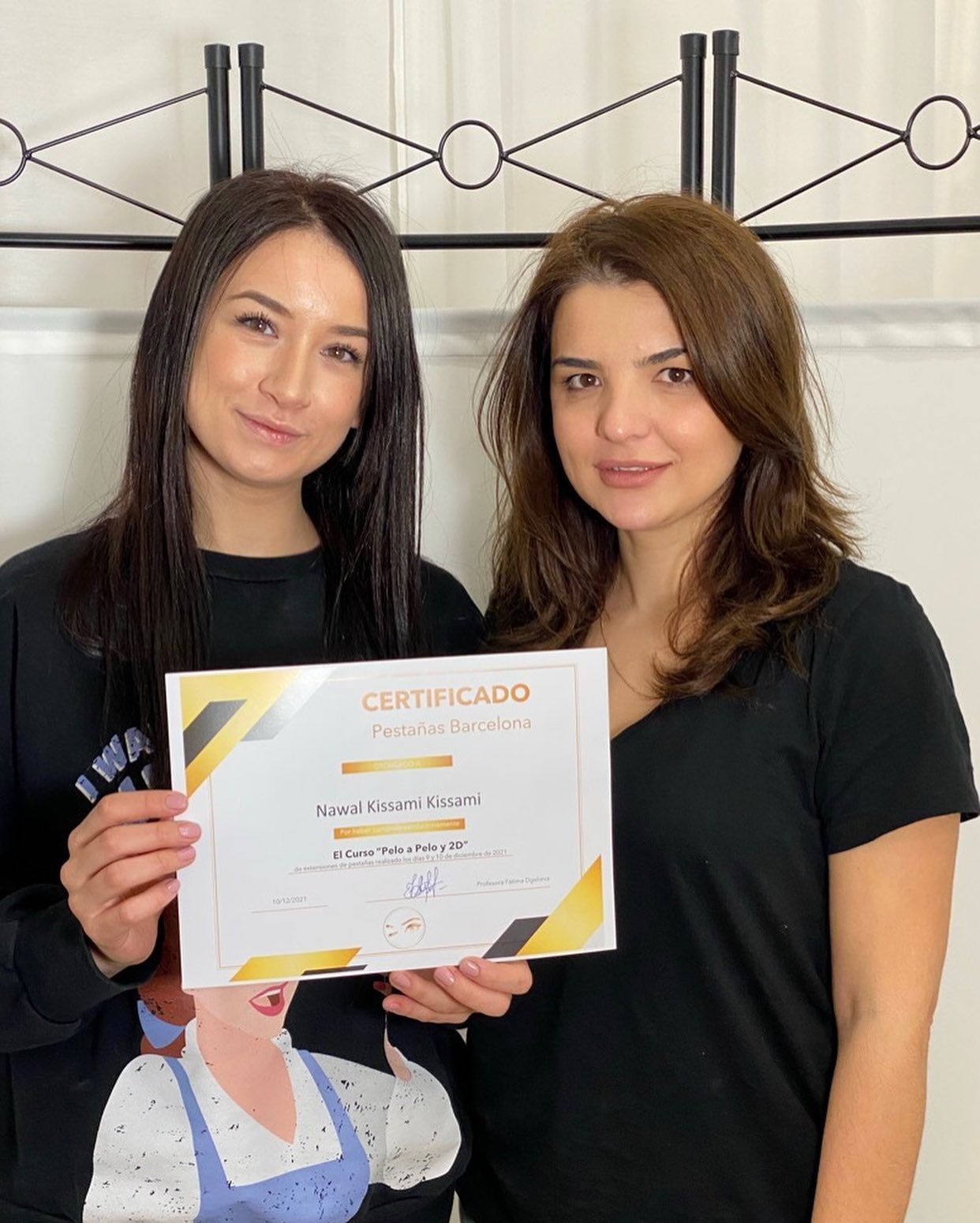 Dos personas de pie una al lado de la otra en el interior de un local; una de ellas sostiene un certificado y ambas sonríen