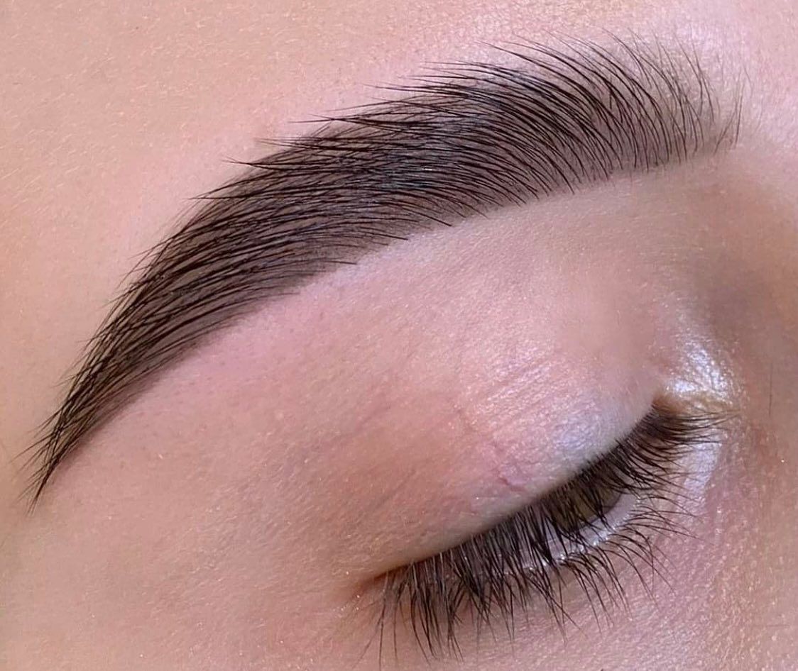 Primer plano de una ceja arreglada y rellena con trazos definidos que imitan el vello.