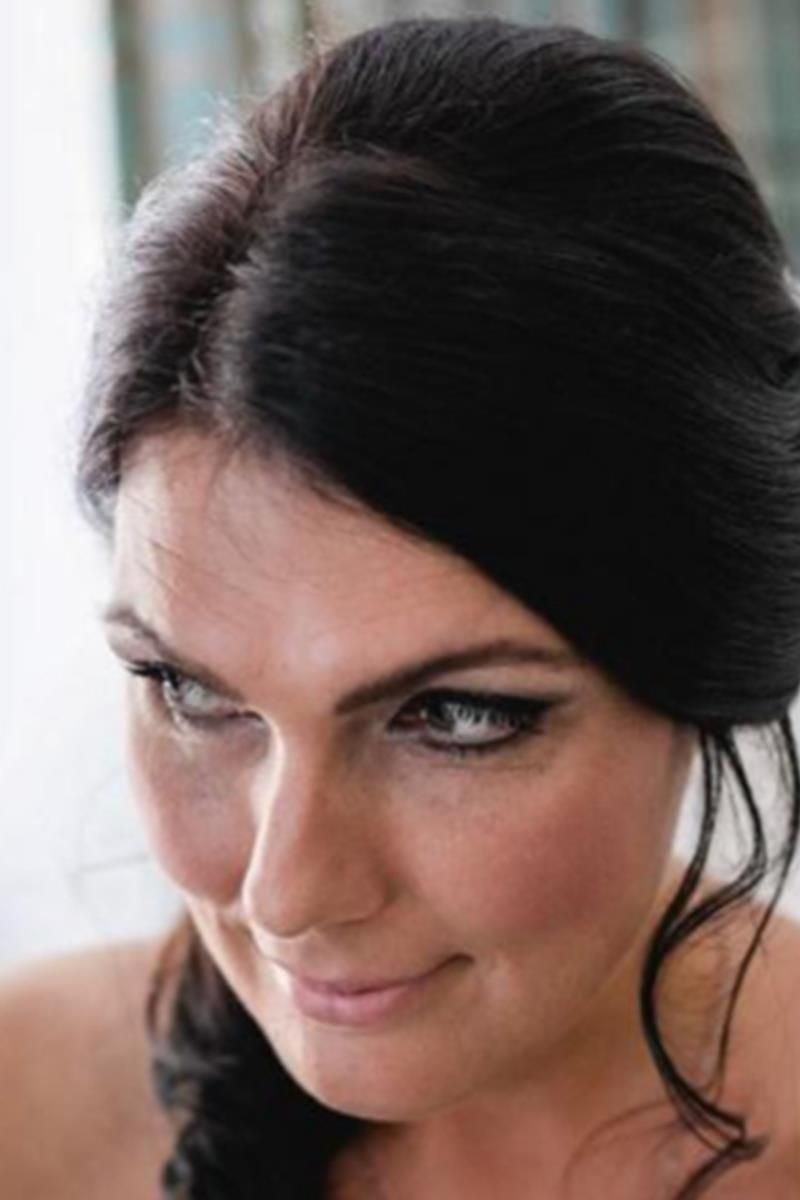 Eine Frau mit langen schwarzen Haaren lächelt und schaut in die Kamera.