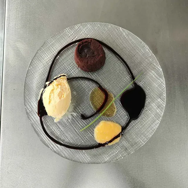 Un plato de vidrio con helado y chocolate encima.